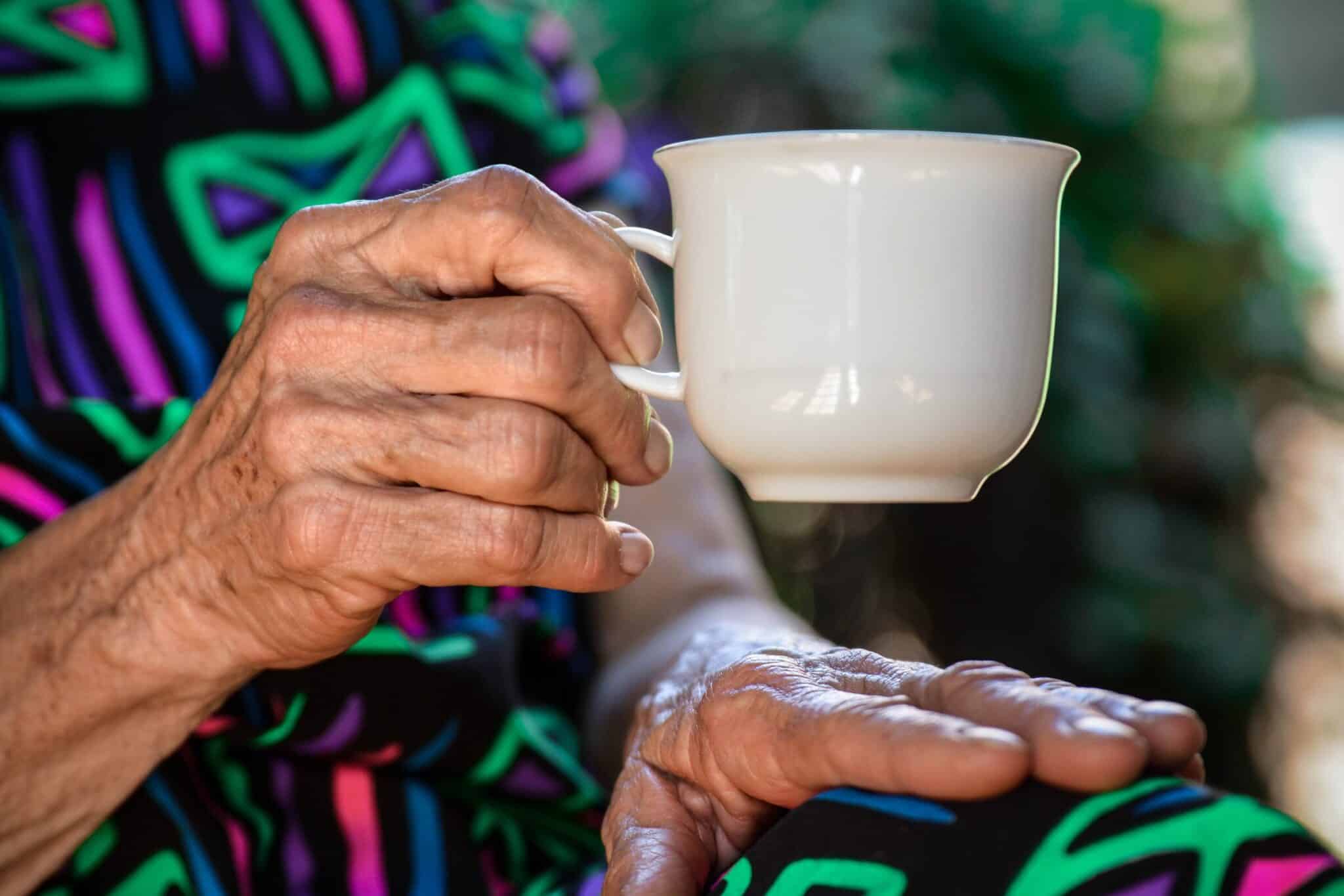 person holding white ceramic teacup to illustrate an older person in their own home
